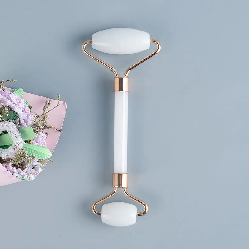 White jade facial roller and gua sha board set on a neutral background.
