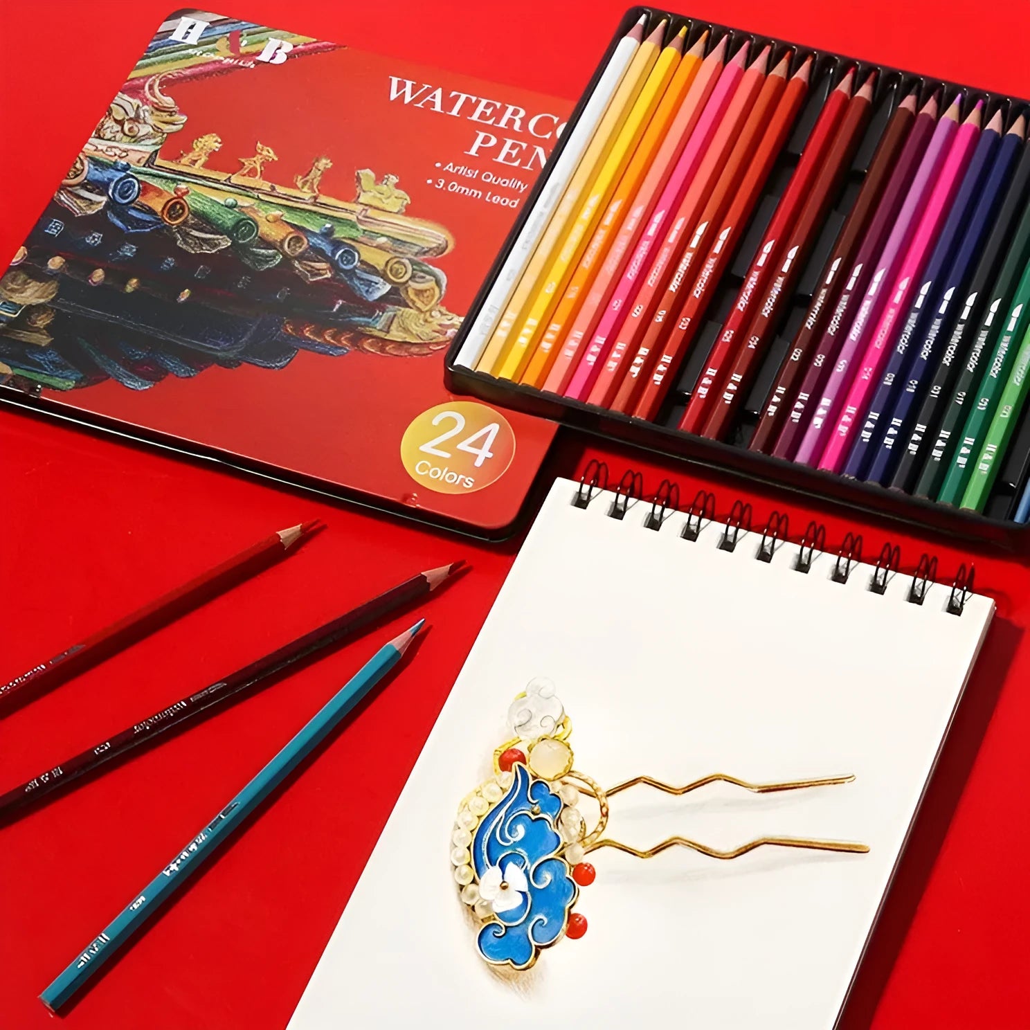 Metal tin box open to show 24 wooden water-soluble coloured pencils in assorted colours.