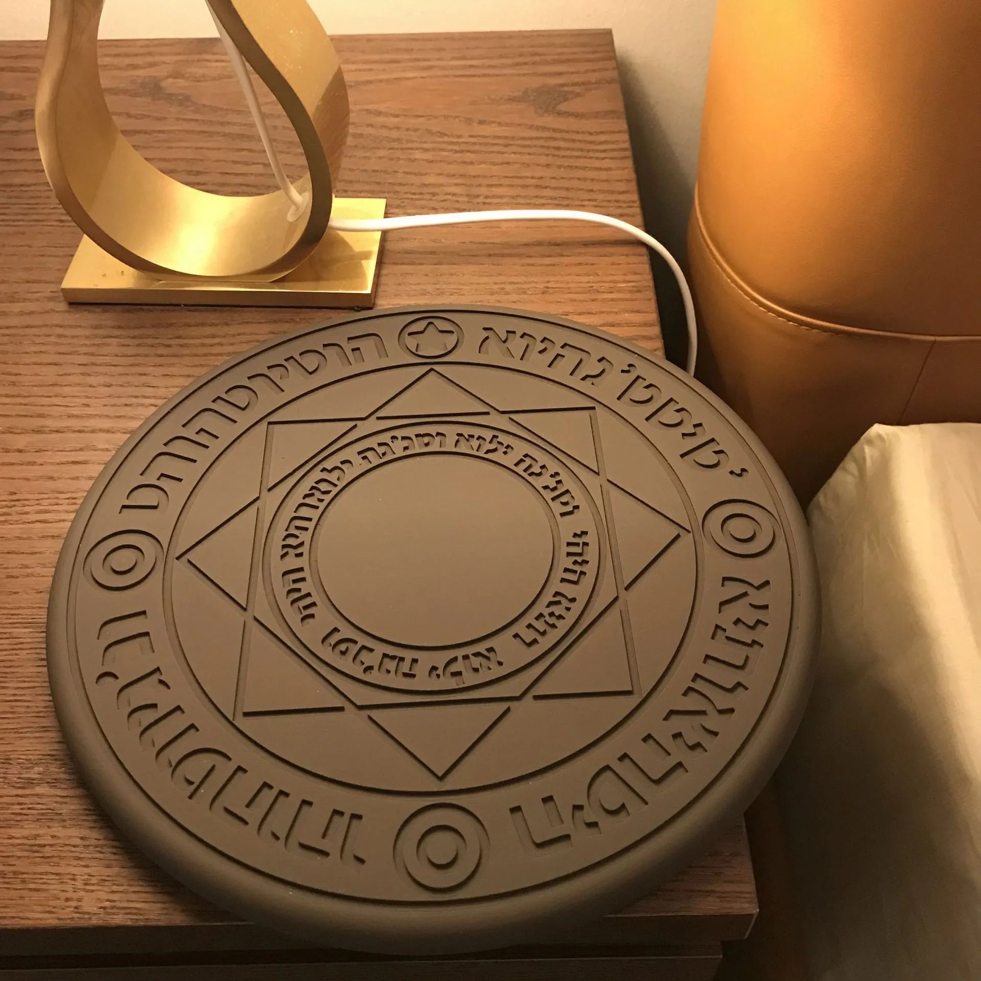 Square black wireless charging pad with illuminated magic array pattern, shown with a smartphone on top.