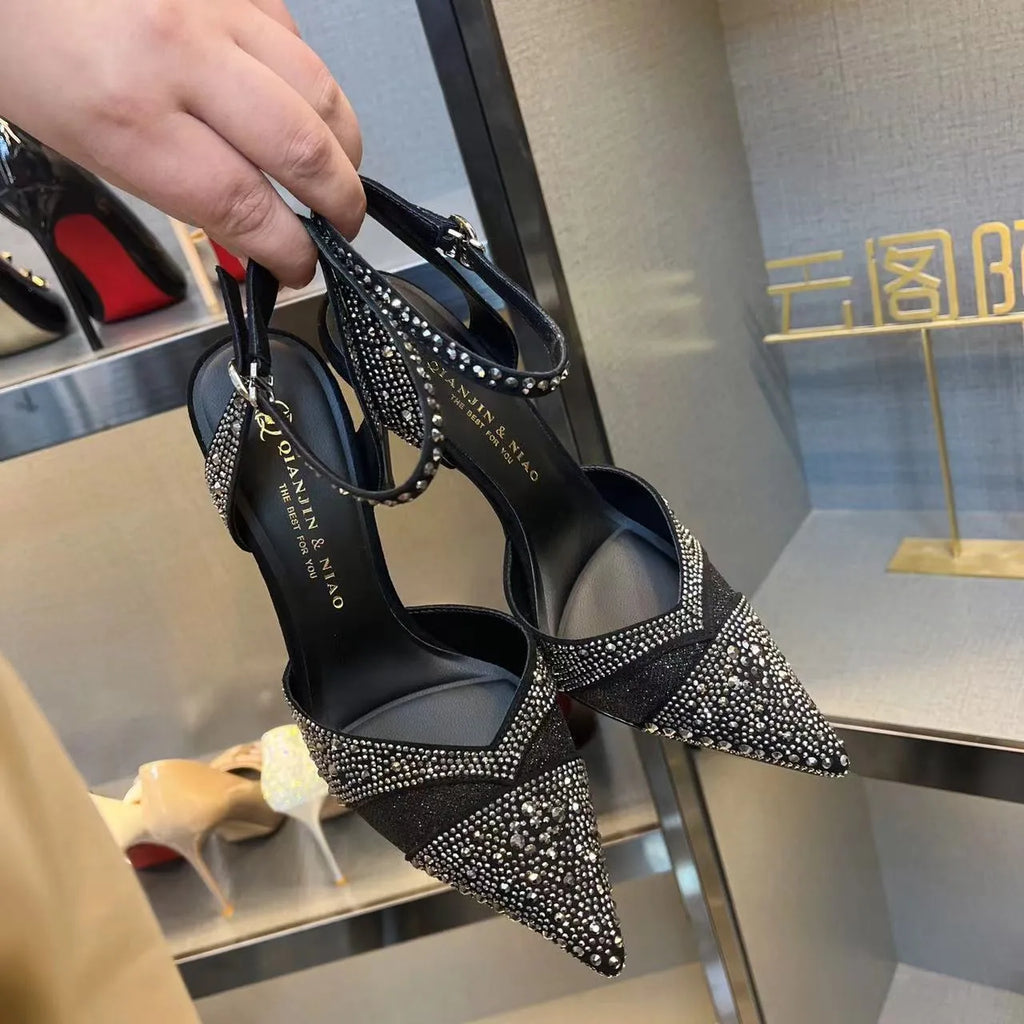 Women's black high heel shoe with pointed toe, stiletto heel, red sole, and hollow design detail.