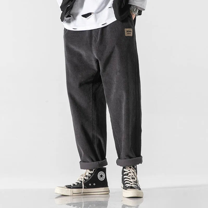 Men's loose straight corduroy sports trousers in black, front view, lying flat, showing waist and leg cut