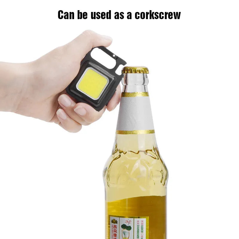 Black aluminium alloy COB keychain flashlight on a metal surface, magnetic base attached, 6x4.2cm size, with foldable handle extended