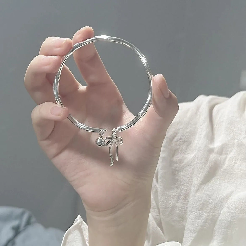 Silver adjustable bracelet with bow charm and small bell detail on wrist