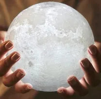 3D printed white moon lamp with detailed craters on a wooden stand, glowing with warm yellow light.
