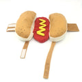 A small dog wearing a brown and beige plush hot dog costume with openings for head, legs, and tail.