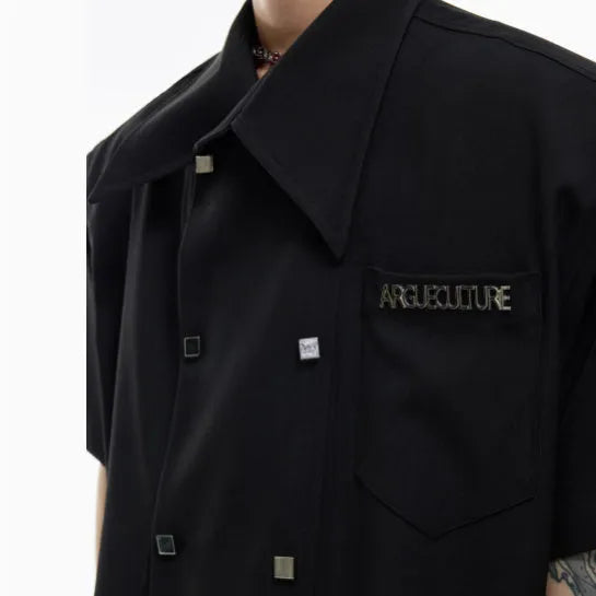 Man wearing a loose-fit short-sleeved casual shirt in blue with a lapel collar and metal button detail.