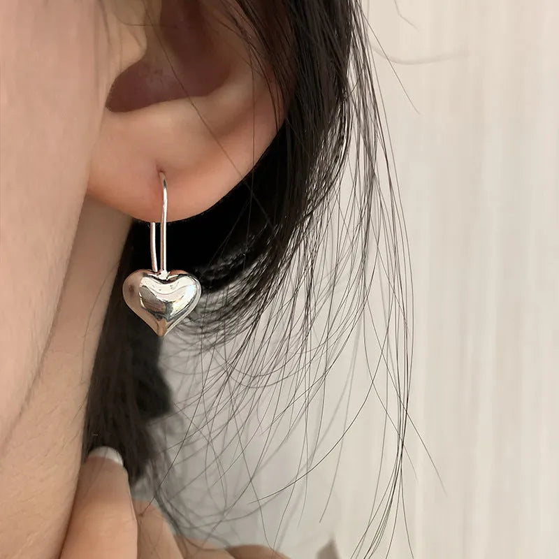 Close-up of glossy silver three-dimensional heart-shaped earrings on a white background.