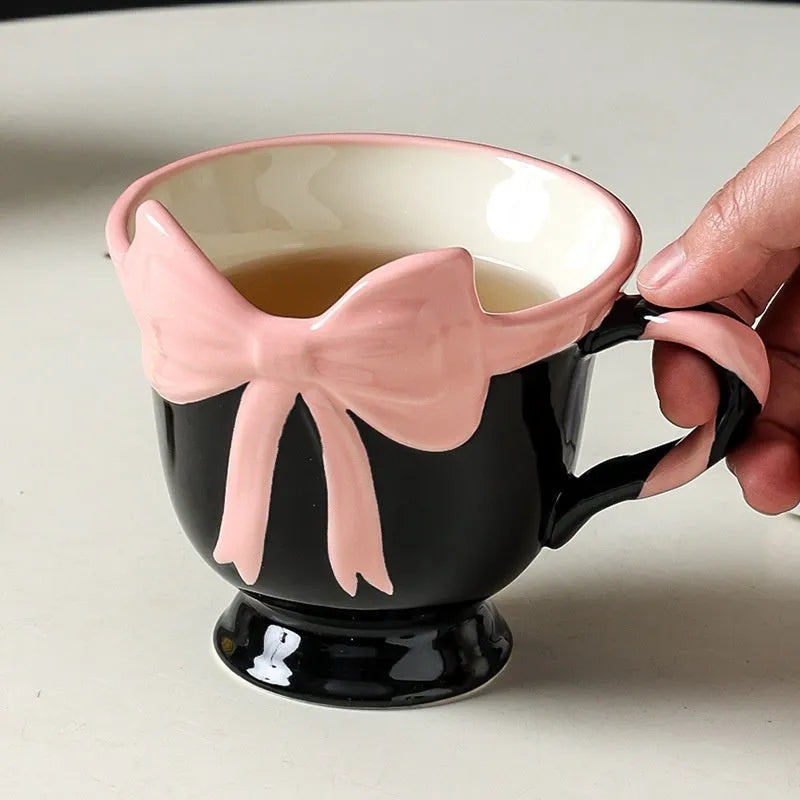 White ceramic mug with a pink heart and black bow design, 350ml capacity.