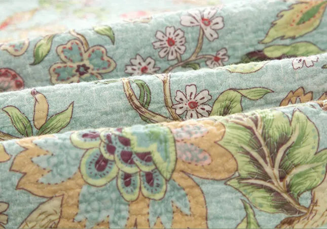 Blue cotton bedspread set with American floral and bird pattern laid on a bed.