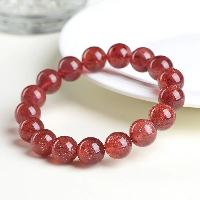 Natural red strawberry quartz crystal bracelet with geometric beads showing a starlight effect, laid flat.