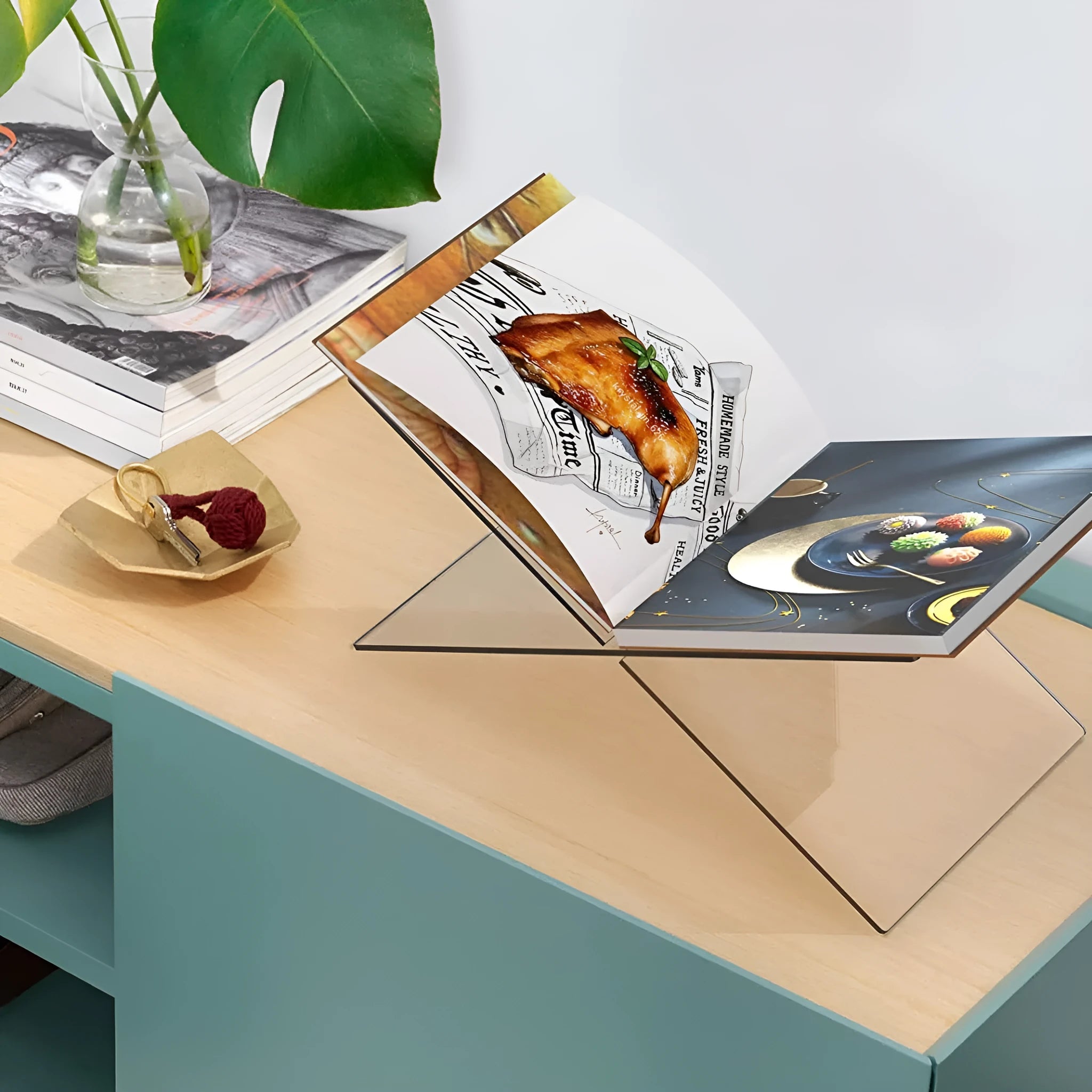 Clear acrylic X-shaped book reading rack displaying hardback books on a wooden desk