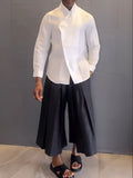 White asymmetric long sleeve shirt with black pleated pants set on a model for casual wear