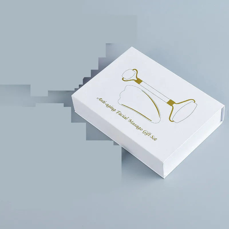 White jade facial roller and gua sha board set on a neutral background.
