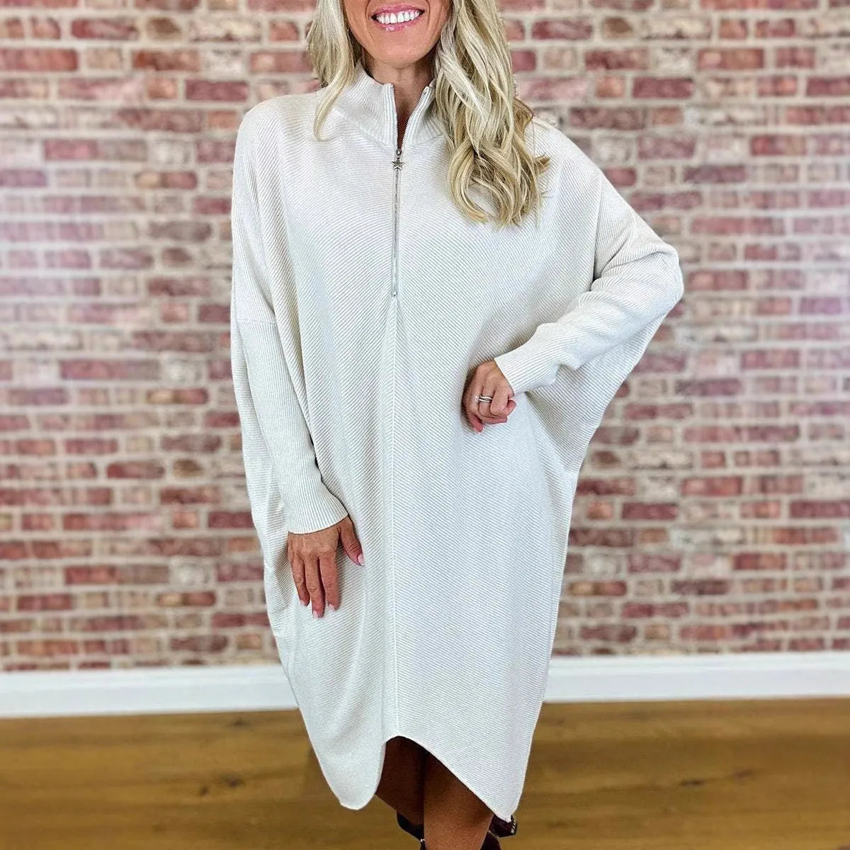 A woman modelling a loose-fitting dark green knitted dress with a front zipper detail and raglan sleeves.