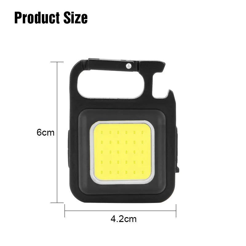 Black aluminium alloy COB keychain flashlight on a metal surface, magnetic base attached, 6x4.2cm size, with foldable handle extended