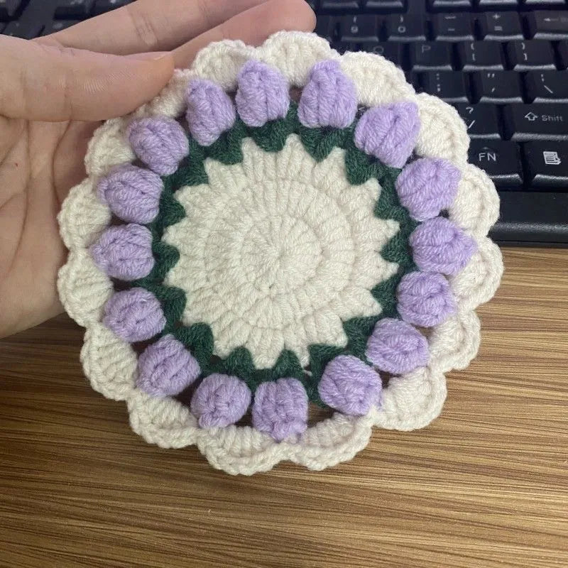 Handmade yarn hook woven flower coaster in pink on a wooden table next to a glass of water