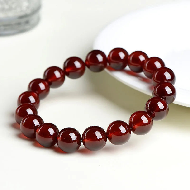 Natural orange red garnet ball bracelet with a silver ruyi charm on a white background.