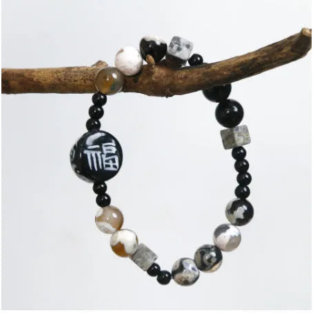 Hand-woven natural glitter stone black agate ceramic bracelet with round geometric beads on a neutral background
