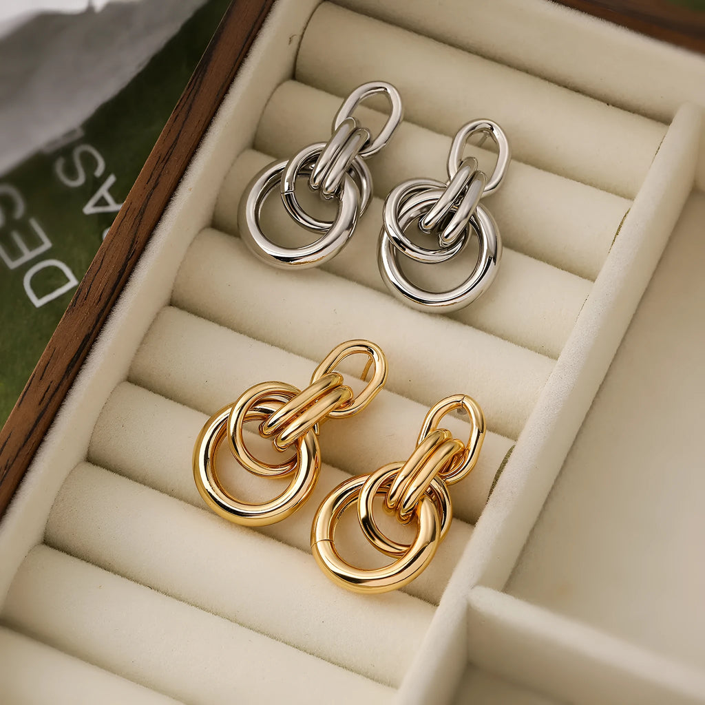 A pair of gold-coloured geometric copper earrings with irregular shapes on a white background.