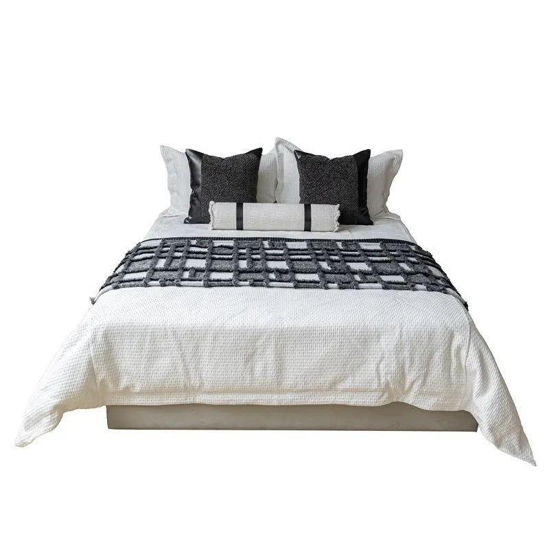 Grey and white plaid bed runner blanket with leather round pillow on bed