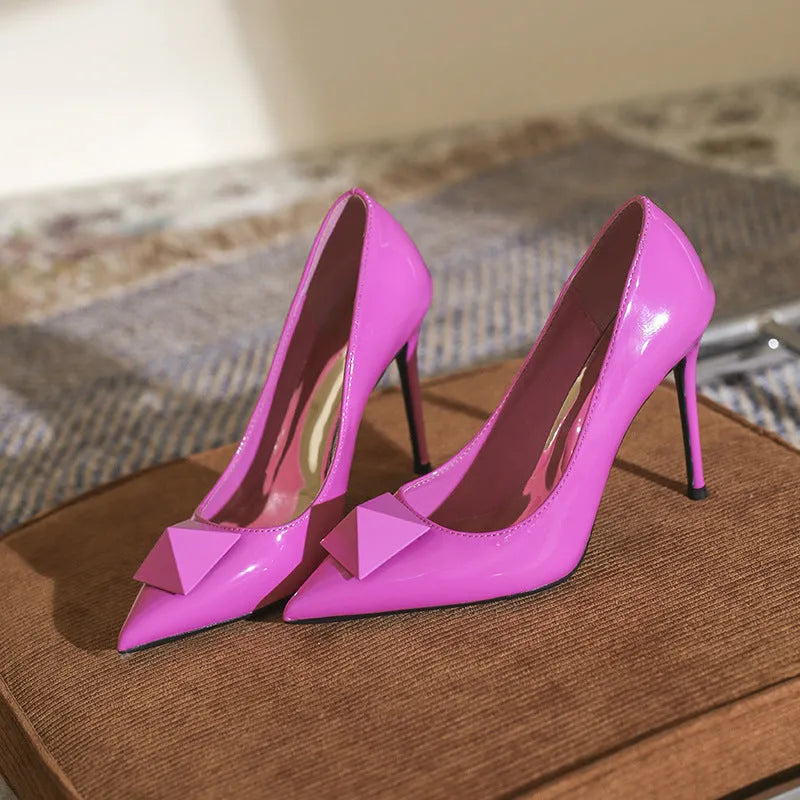 Pink women's patent leather pointed toe stiletto heels with a buckle, shown on a white background.