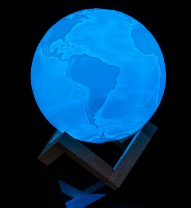3D printed white moon lamp with detailed craters on a wooden stand, glowing with warm yellow light.