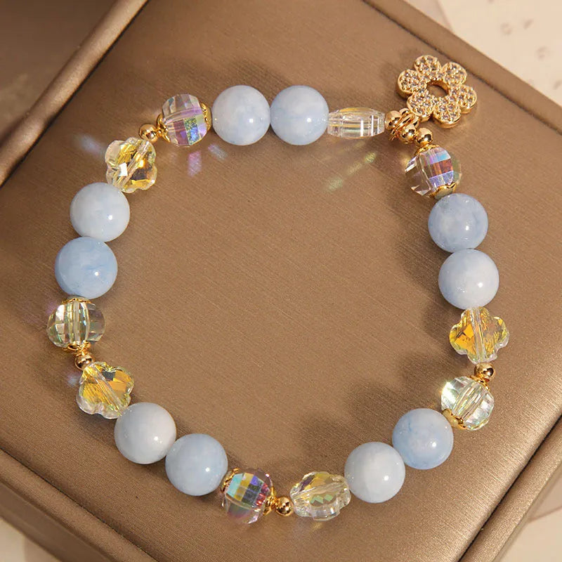 Women's aquamarine crystal bracelet with four-leaf clover design and pearl accents on a wrist.