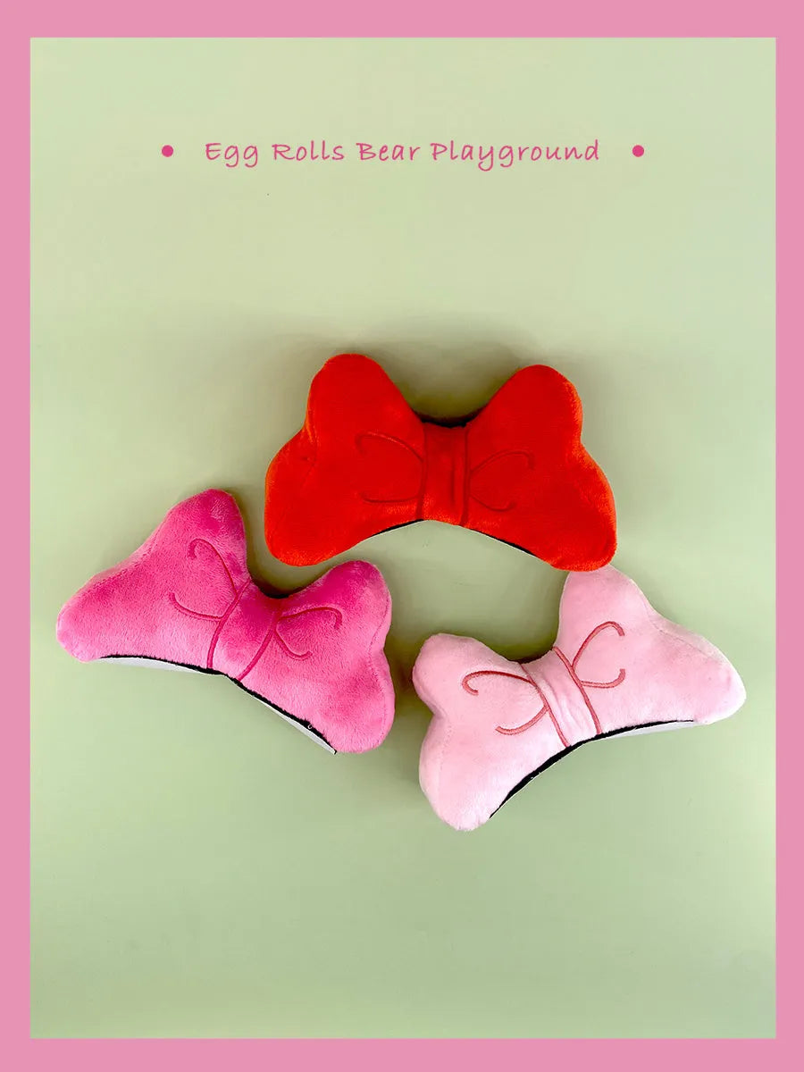 Plush bow tie helmet decoration in red, peach pink, and rose pink colours shown on a motorcycle helmet.