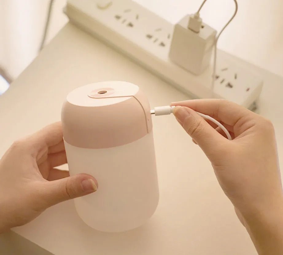 White cylindrical USB mini humidifier with charging cable on desk