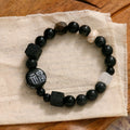 Hand-woven natural glitter stone black agate ceramic bracelet with round geometric beads on a neutral background