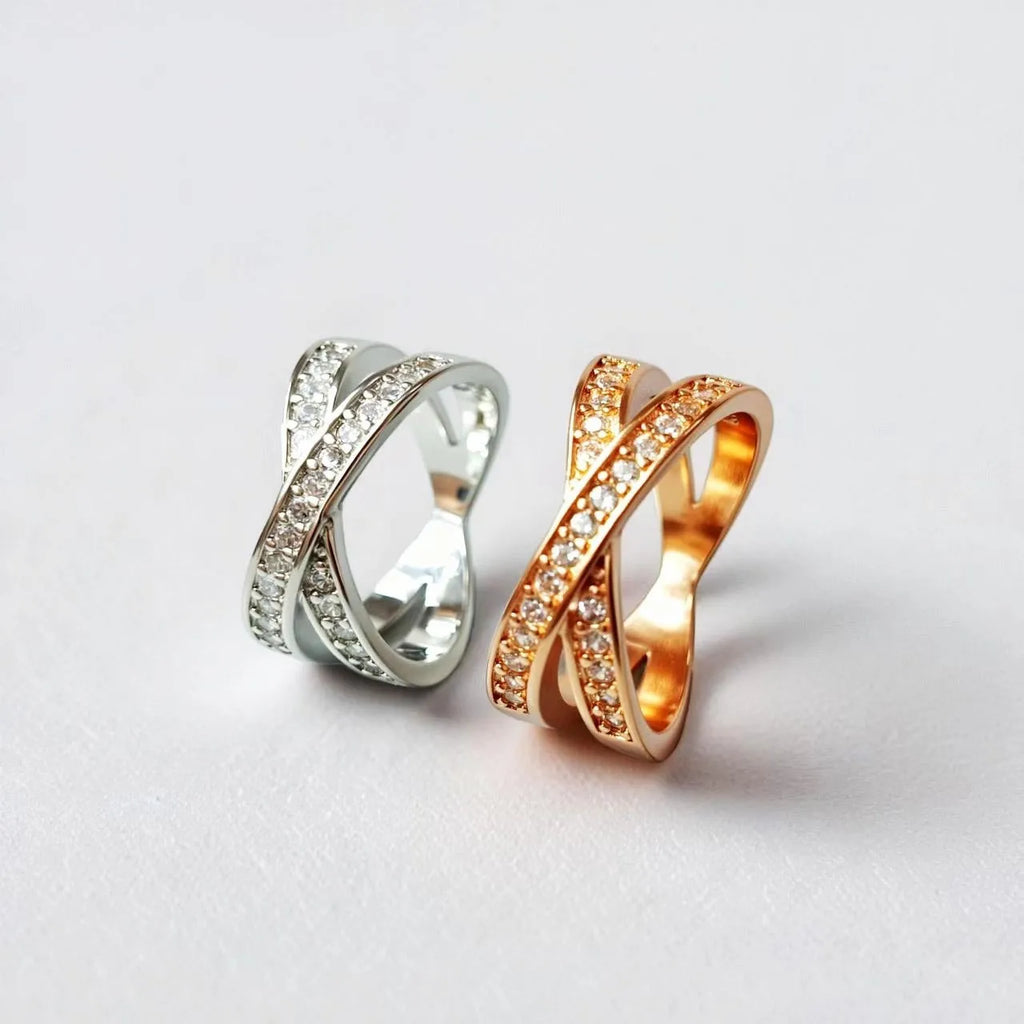 A silver or rose gold metal ring featuring a central cross design with small zircon stones.