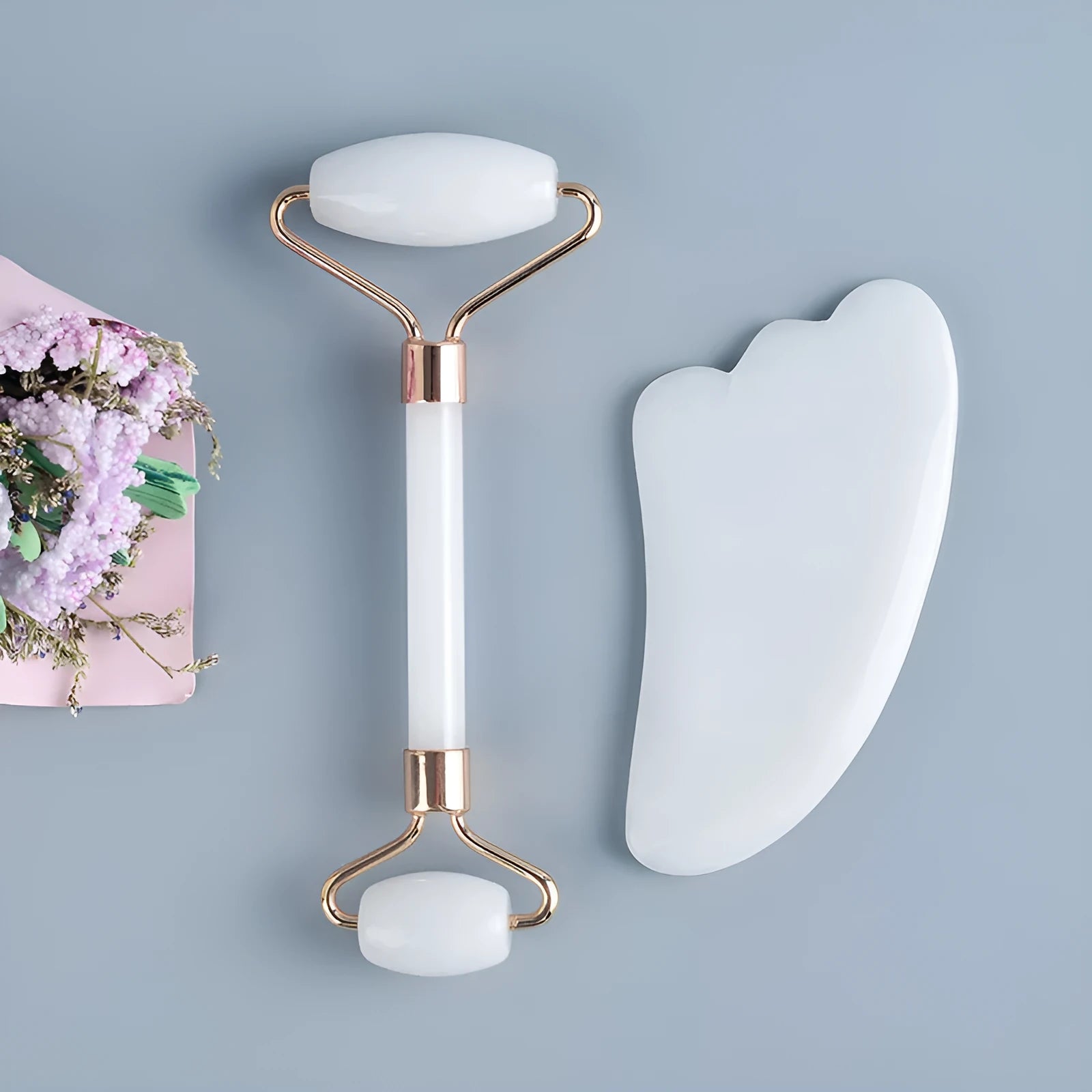 White jade facial roller and gua sha board set on a neutral background.