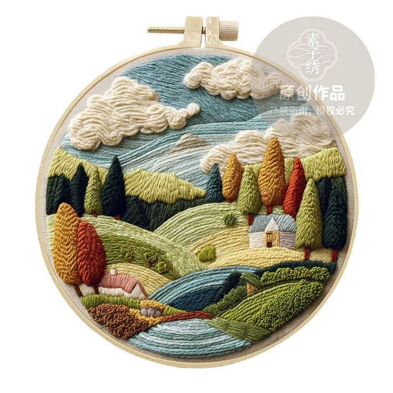 Embroidery DIY kit with cotton landscape fabric, bamboo frame, threads, and tools on wooden surface
