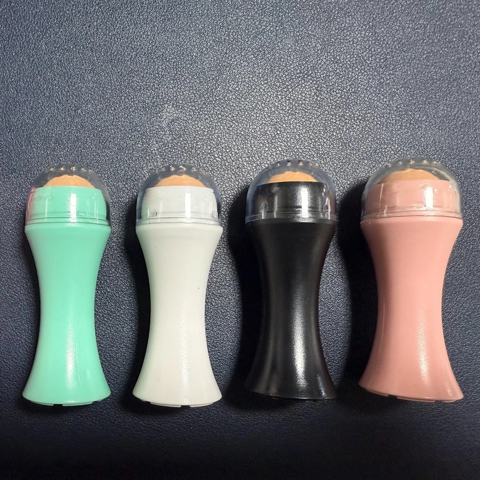Volcanic stone facial roller for oily skin in black, green, pink, or white on a plain background