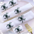 Six black alloy spider-shaped napkin rings for Halloween table decoration on a dark surface.