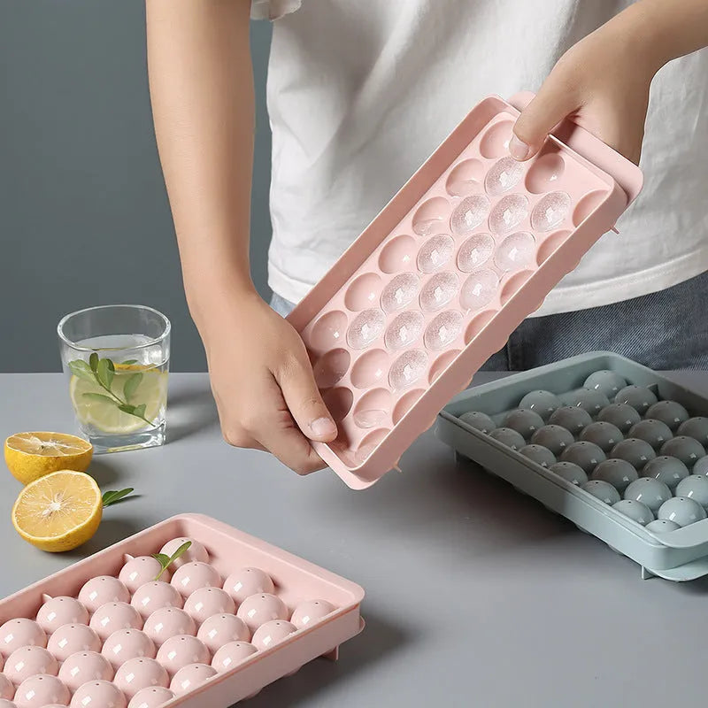 Round ball ice cube tray in sky blue with 33 grids, empty and filled with water, on a kitchen countertop