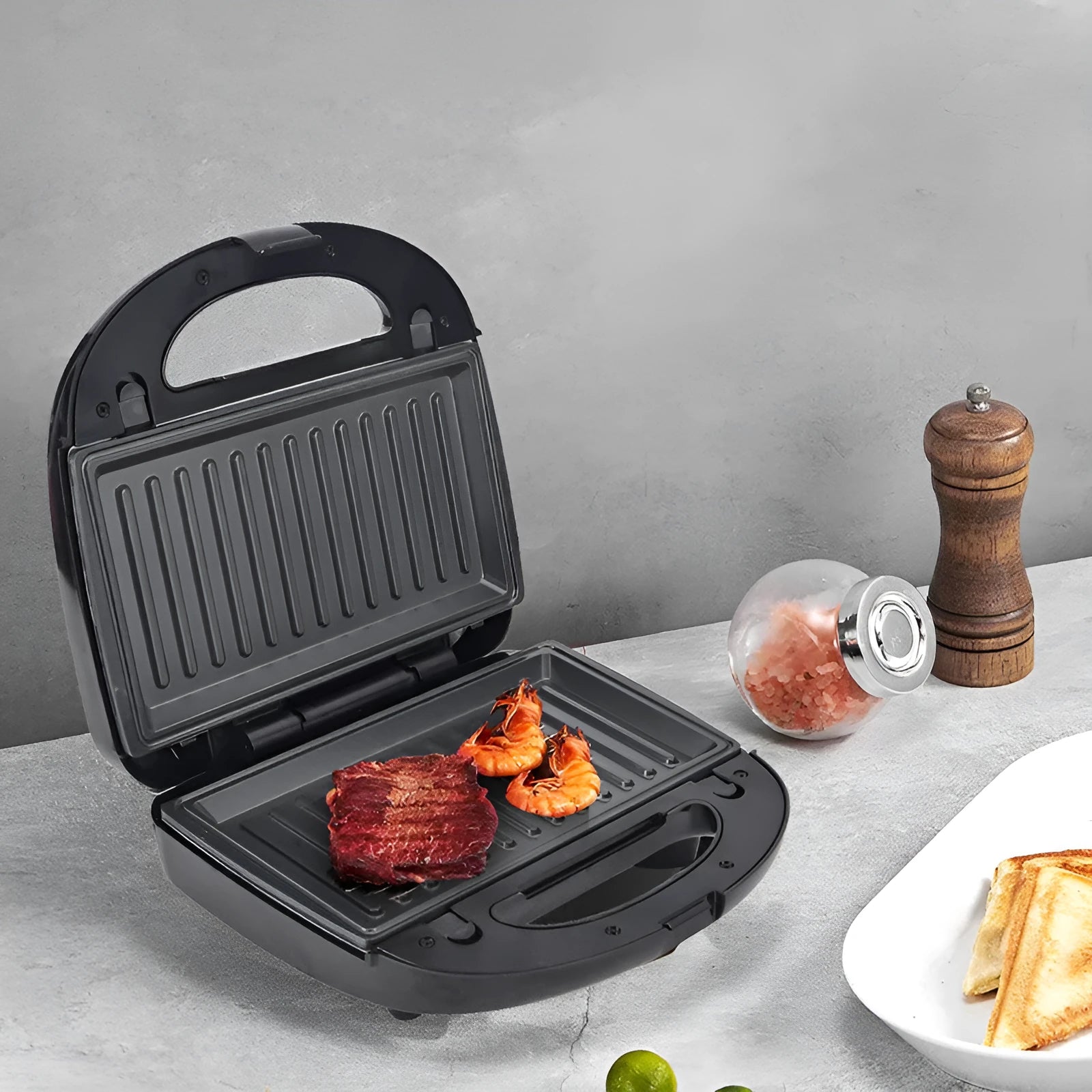 Black double-sided electric sandwich pan with brushed stainless steel cover on a kitchen counter.