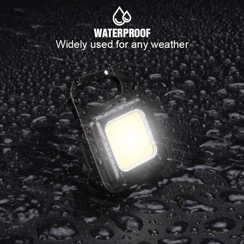 Black aluminium alloy COB keychain flashlight on a metal surface, magnetic base attached, 6x4.2cm size, with foldable handle extended