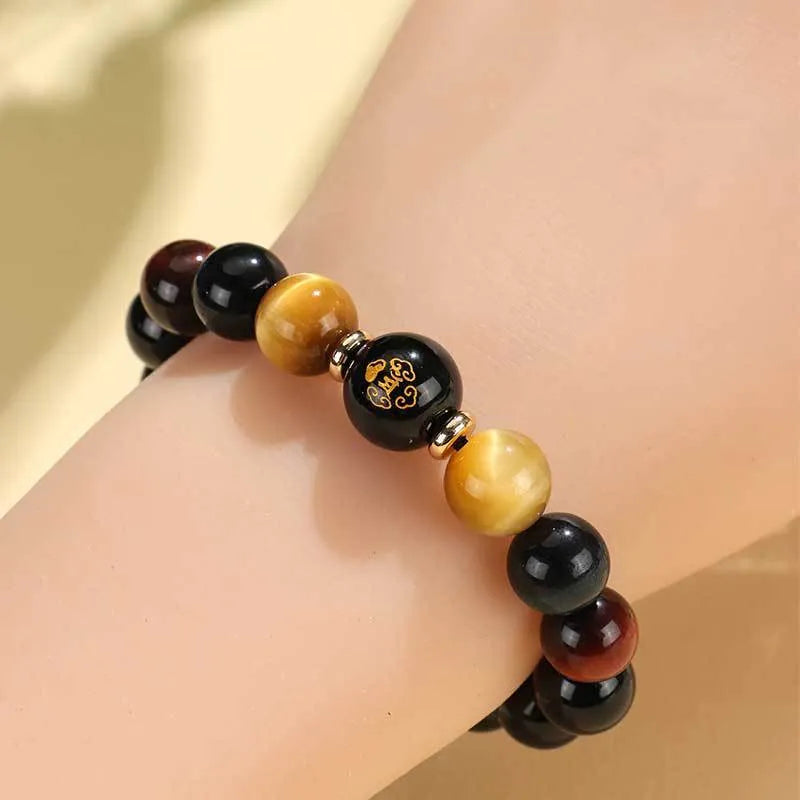 Black agate beaded bracelet with gold tiger eye accent and Chinese zodiac bodhisattva charm on neutral background