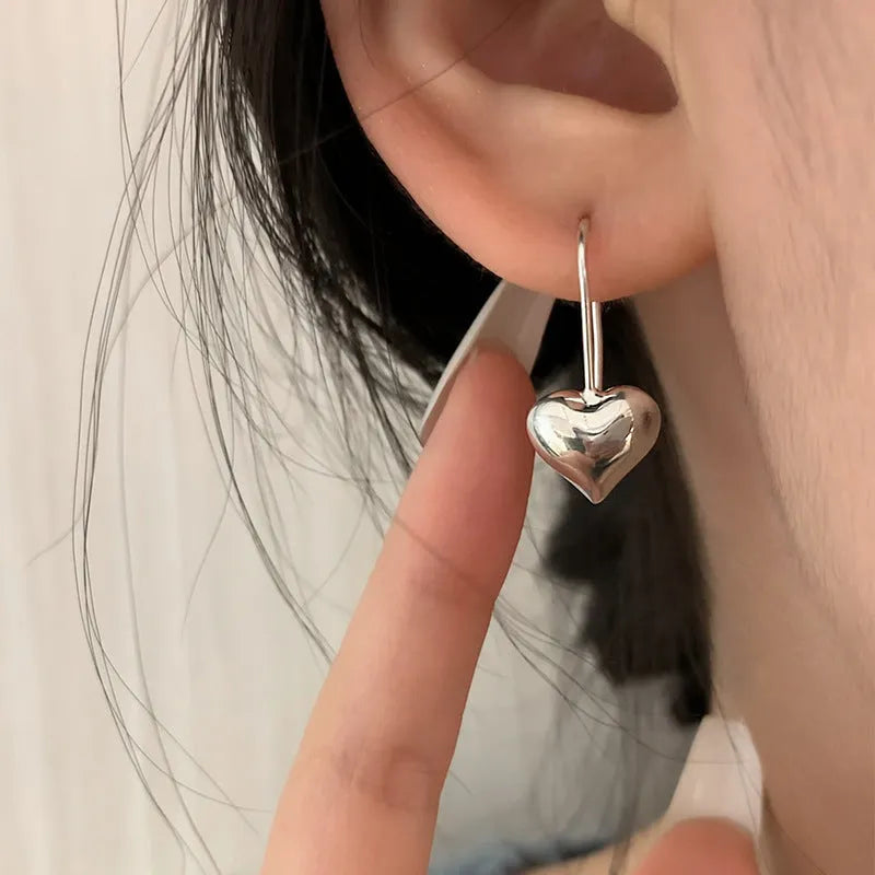 Close-up of glossy silver three-dimensional heart-shaped earrings on a white background.