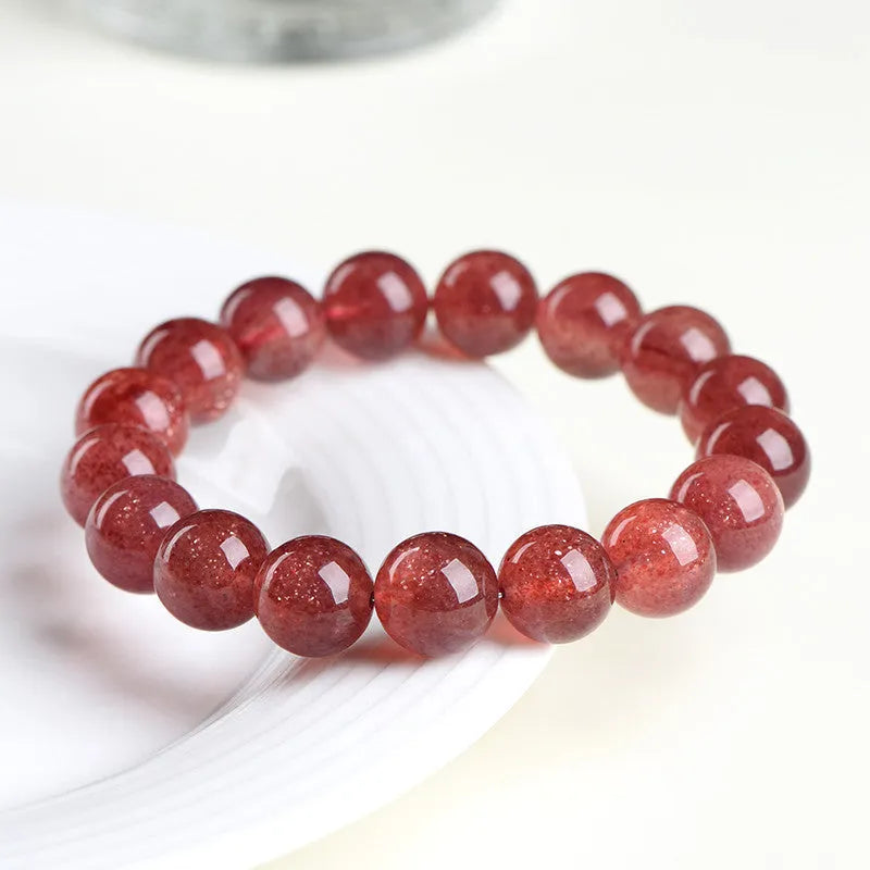Natural red strawberry quartz crystal bracelet with geometric beads showing a starlight effect, laid flat.