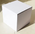 Square corrugated cardboard packaging box in black, shown alongside smaller white and grey boxes.