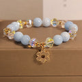 Women's aquamarine crystal bracelet with four-leaf clover design and pearl accents on a wrist.