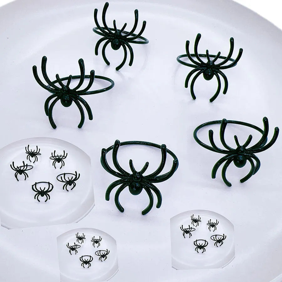 Six black alloy spider-shaped napkin rings for Halloween table decoration on a dark surface.