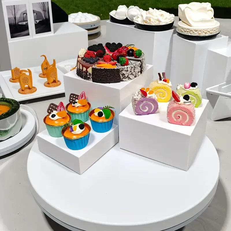 White plastic suit cube stacking dessert display stand with six pieces arranged for cake presentation.