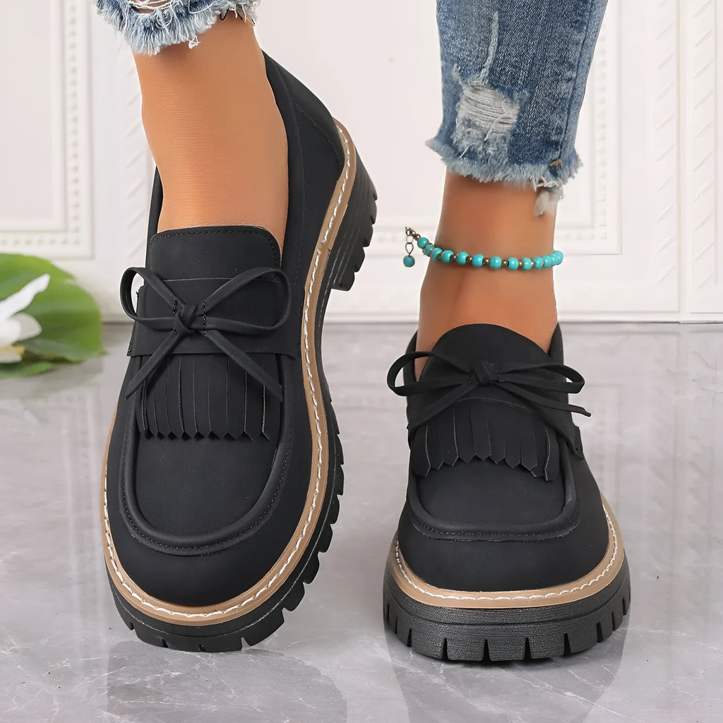 Black plus size women's loafers with a tassel and bowknot on a chunky rubber sole.