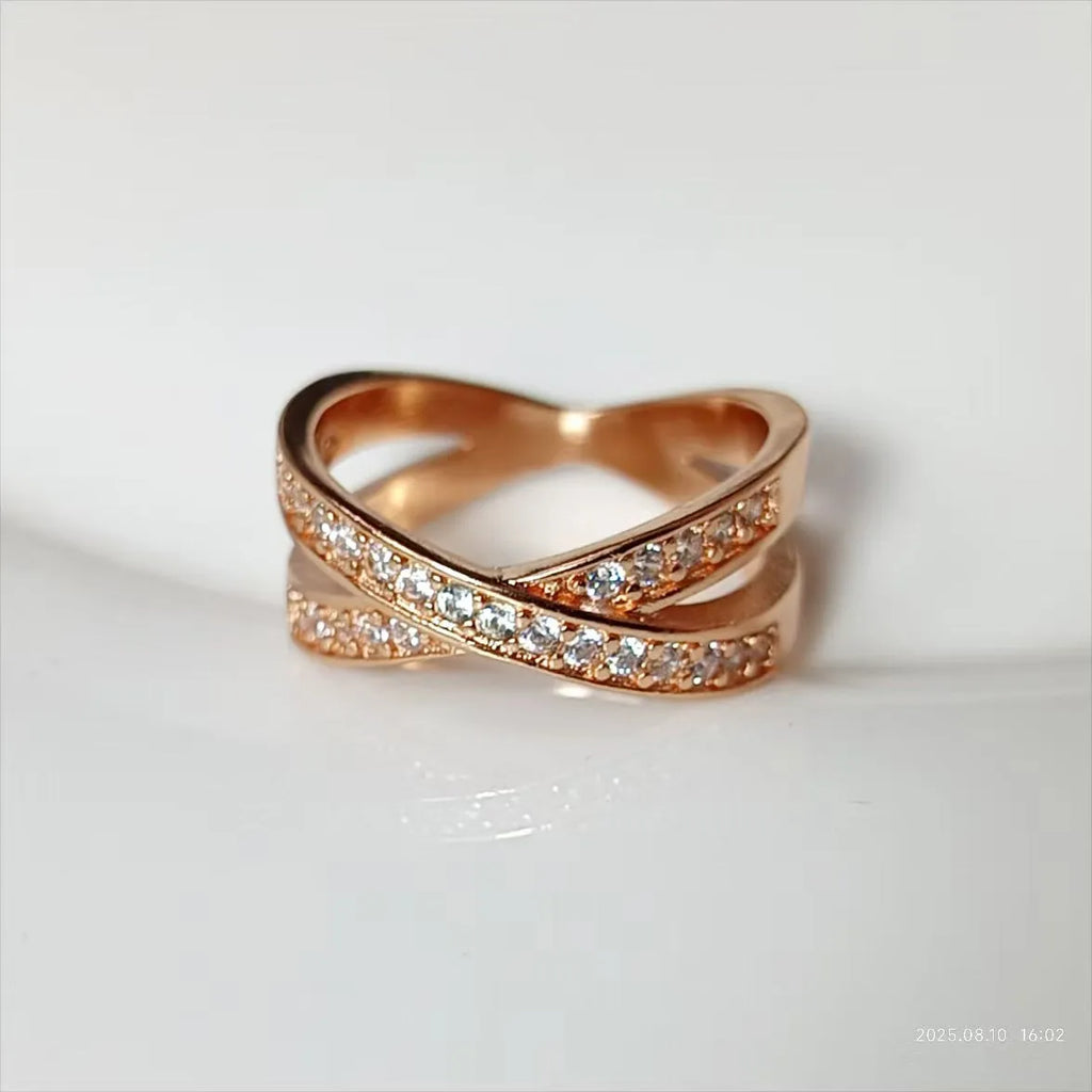 A silver or rose gold metal ring featuring a central cross design with small zircon stones.