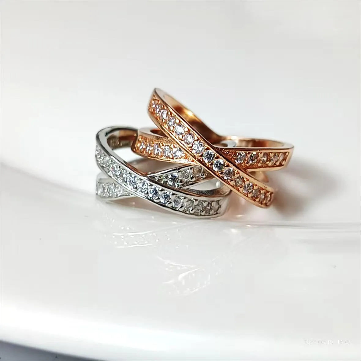 A silver or rose gold metal ring featuring a central cross design with small zircon stones.
