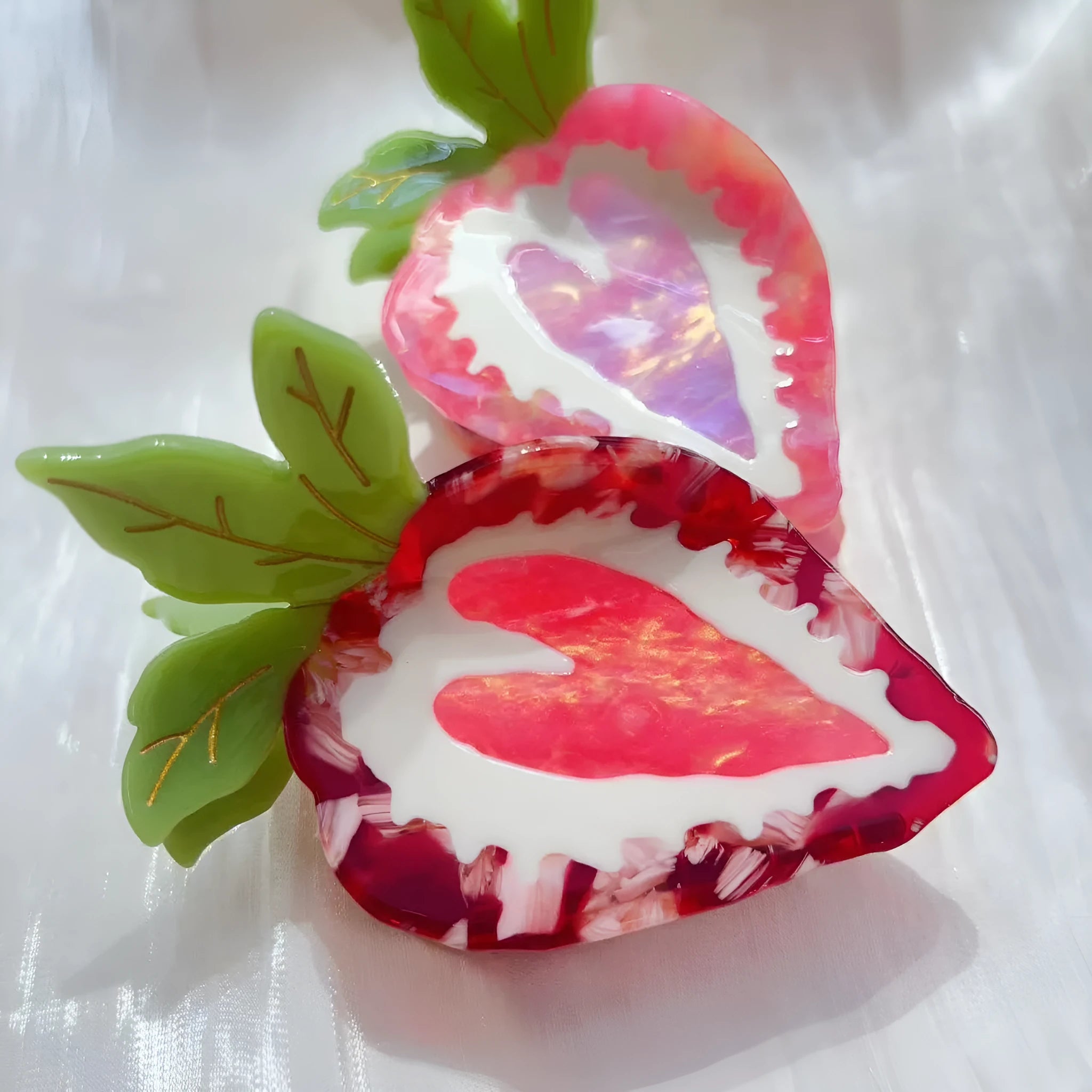 Close-up of a handmade strawberry hair clip in red or pink on a white background.