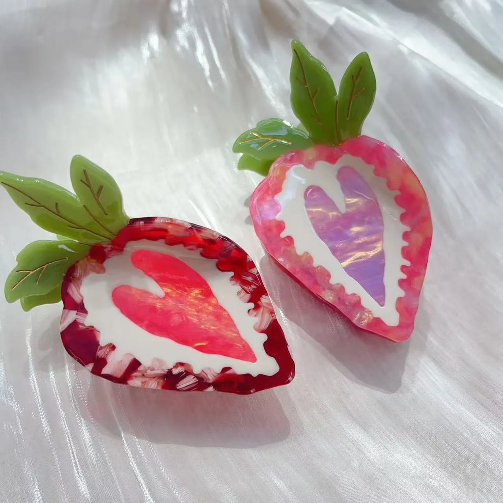 Close-up of a handmade strawberry hair clip in red or pink on a white background.
